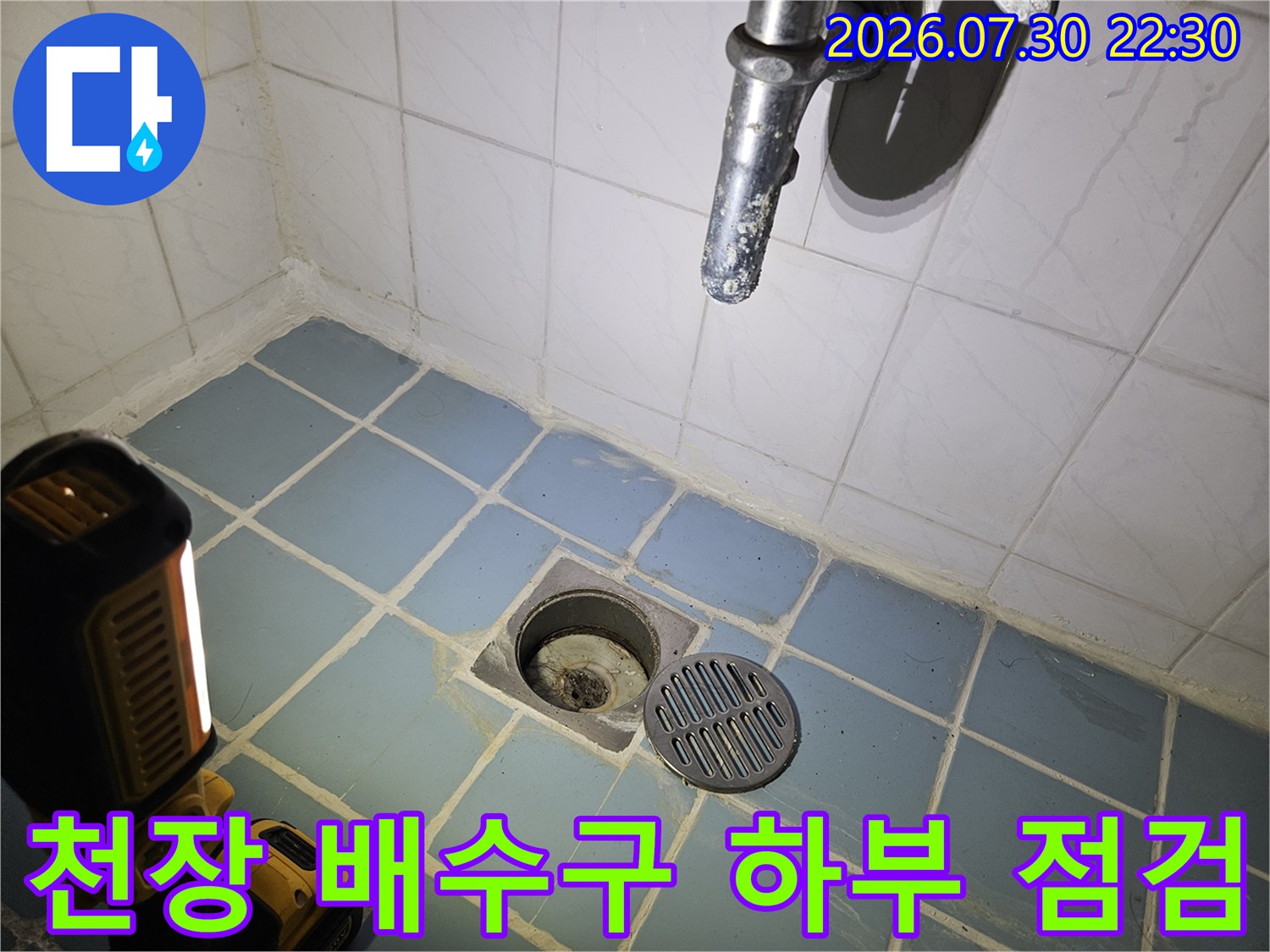 파란색 타일과 대조되는 노출된 배수용 파이프와 주변 오염 부위의 근접 촬영 사진