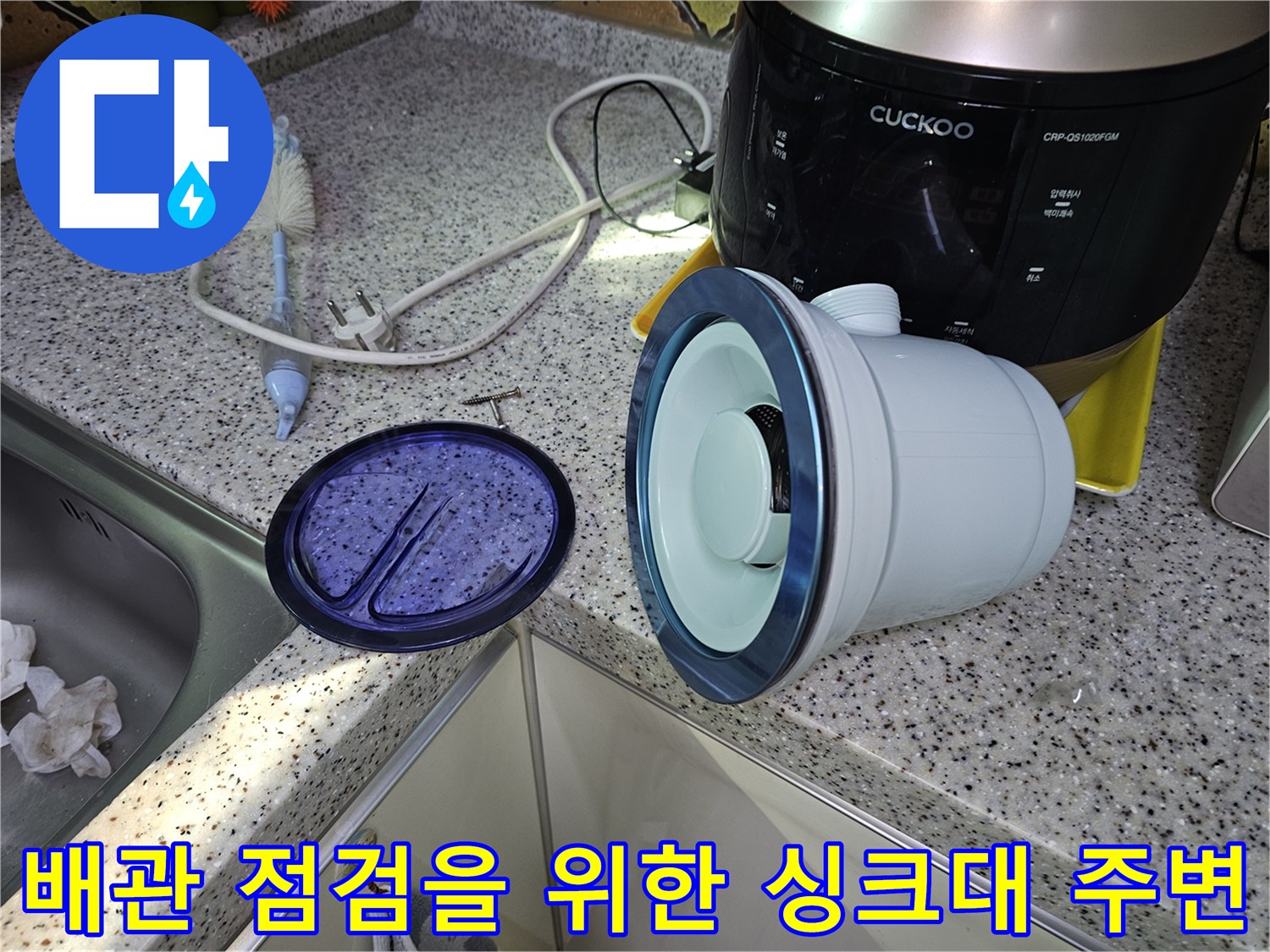싱크대 하부 배관 부품과 밥솥이 놓여 있는 주방 작업 현장입니다.