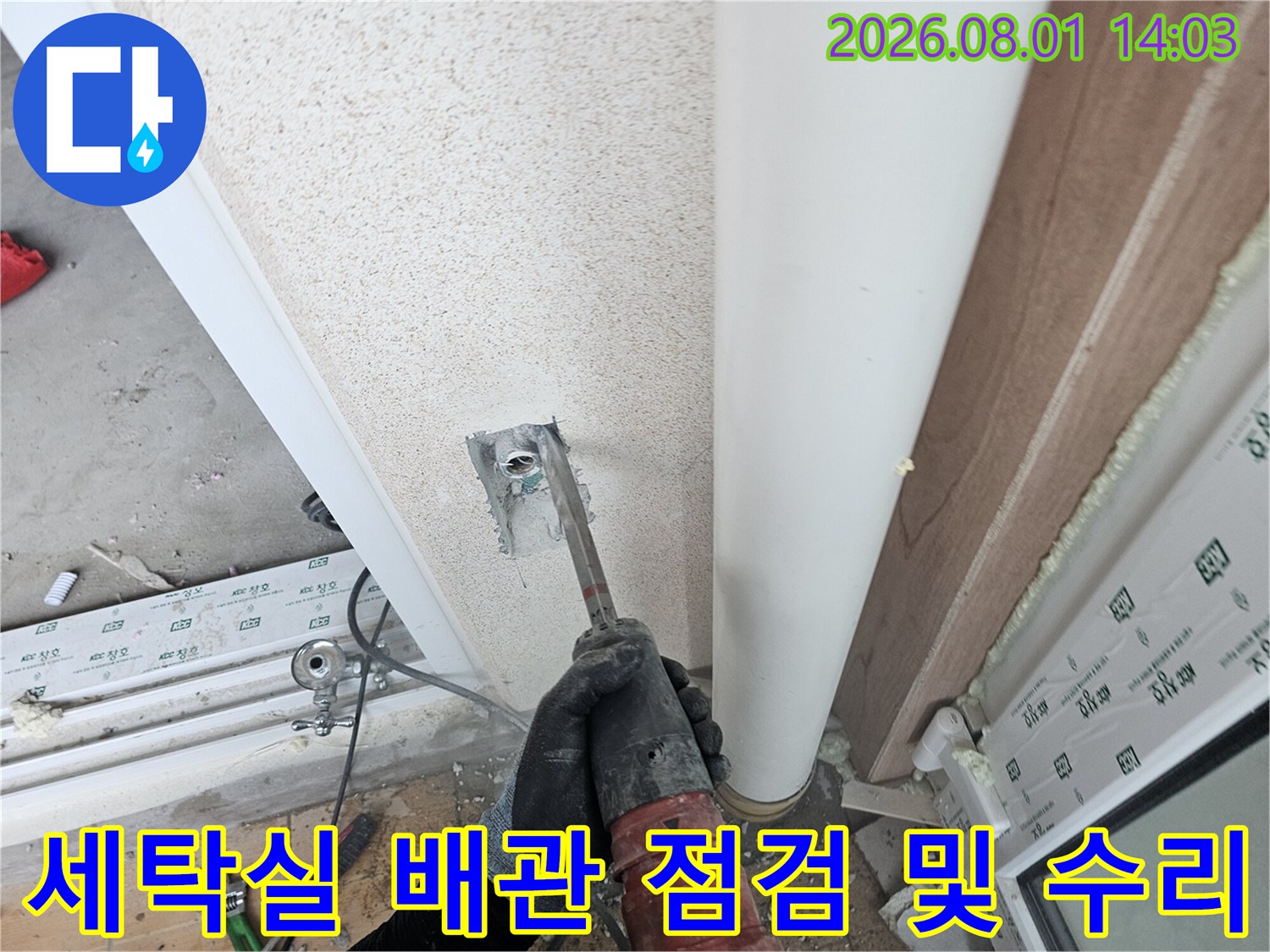 장갑을 낀 채 세탁실 벽면의 노출된 직수 파이프 연결 부위를 도구와 함께 살피는 장면