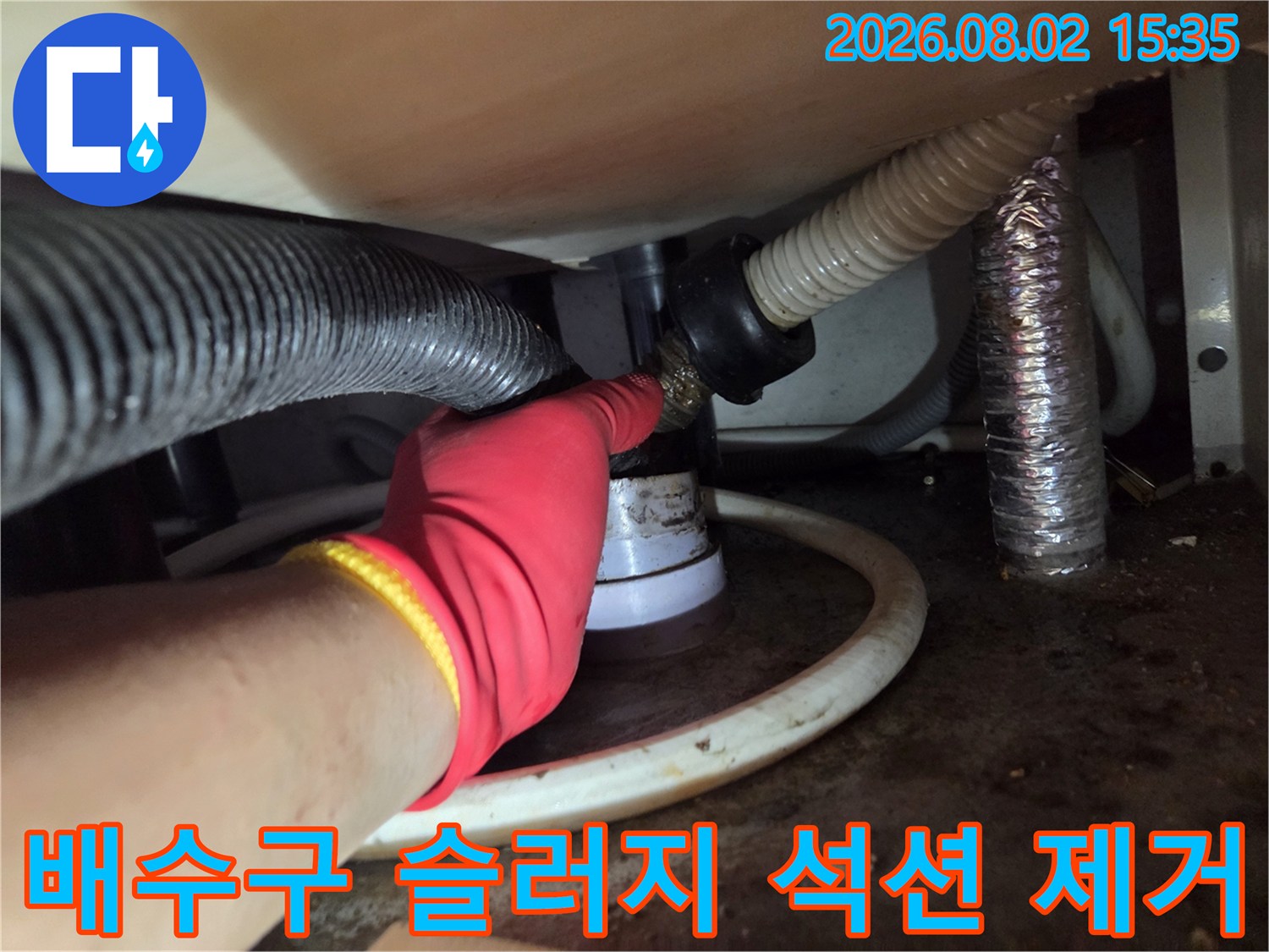노출된 싱크대 하단 배수 트랩 구간에 석션 호스를 연결하여 이물질을 직접 제거하는 모습.