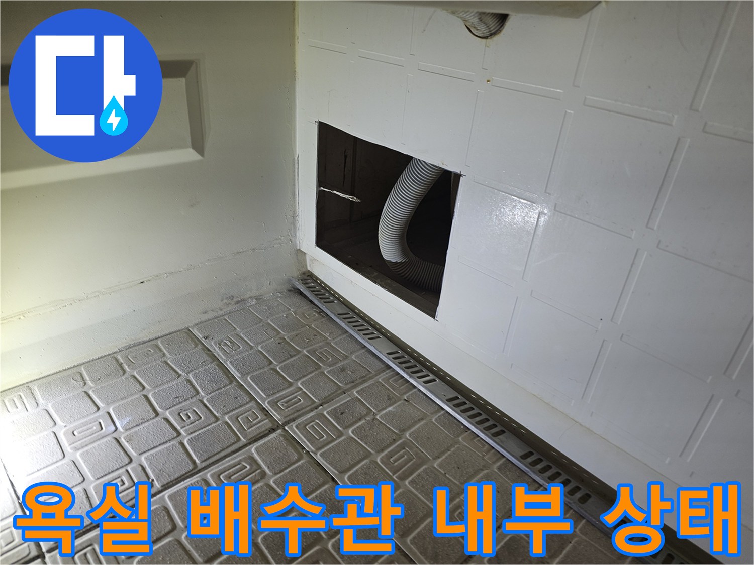 타공된 점검구 사이로 보이는 굴곡진 형태의 배수 호스