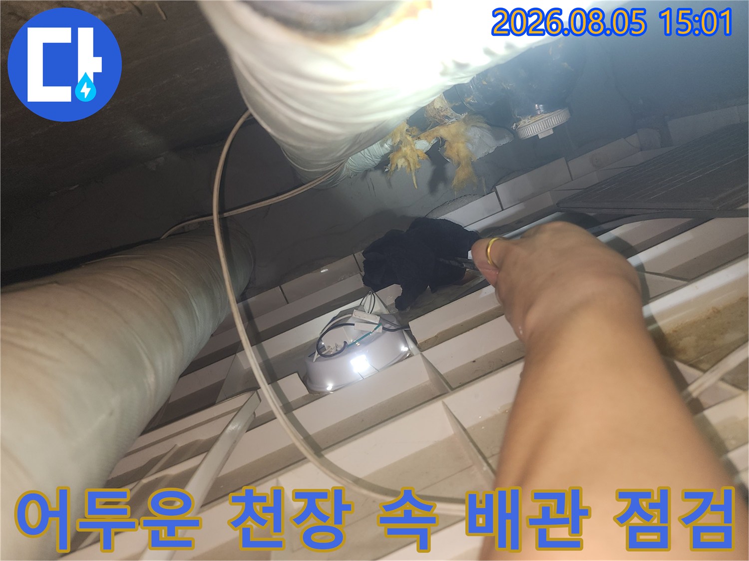조명 장비를 사용하여 어두운 천장 내부 배관 상태를 살피는 작업 모습