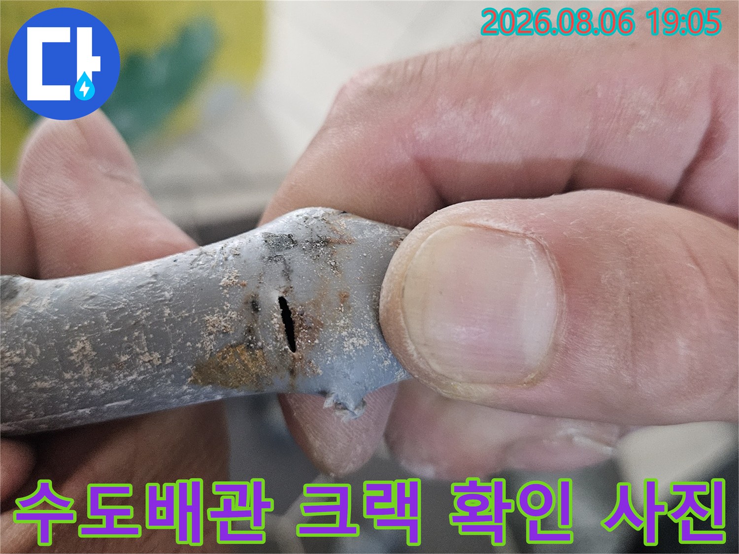 수도배관 표면의 균열 부위를 손으로 가리키며 누수 지점 설명