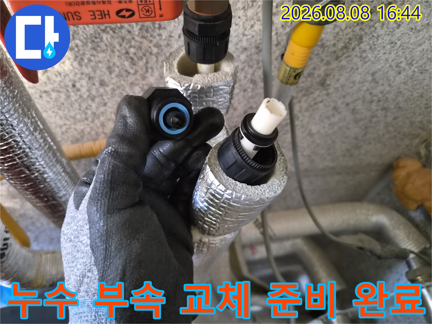 새로운 배관 부속을 쥐고 있는 작업자의 손과 기존 배관 모습