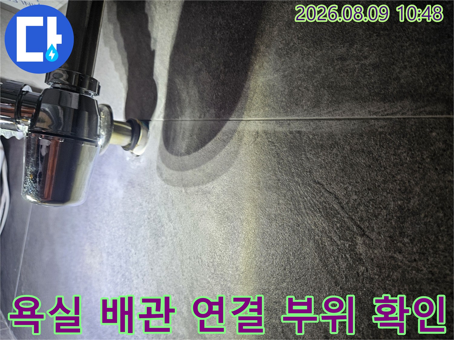 어두운 욕실 타일 벽면의 배관 연결 부위를 가까이서 촬영한 모습입니다.