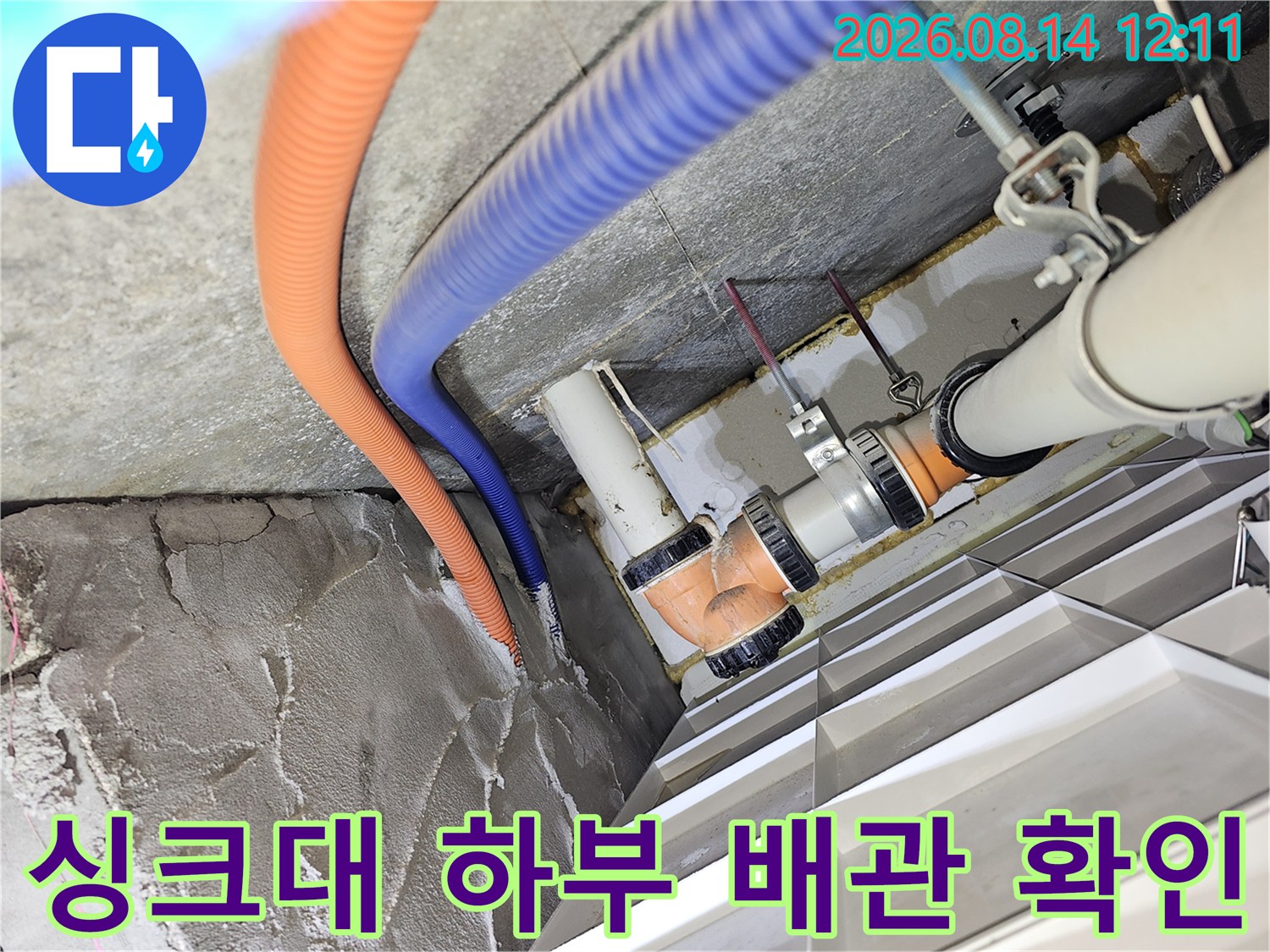 싱크대 아래 천장 공간 - 오렌지색 주름관과 PVC 배관의 연결 상태 확인 중