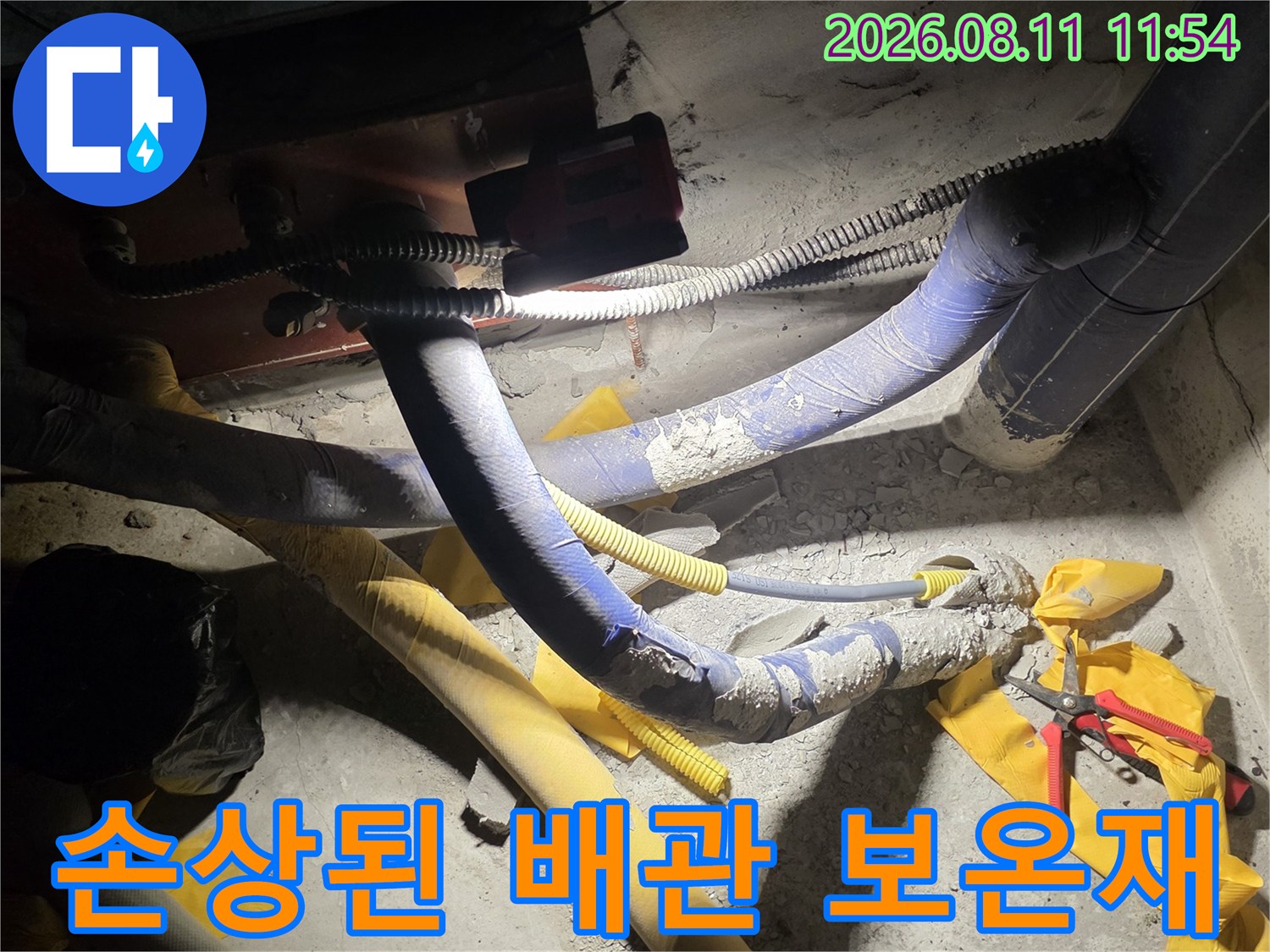 배관을 감싸고 있는 파란색 보온재와 노란색 테이프가 손상된 모습입니다.