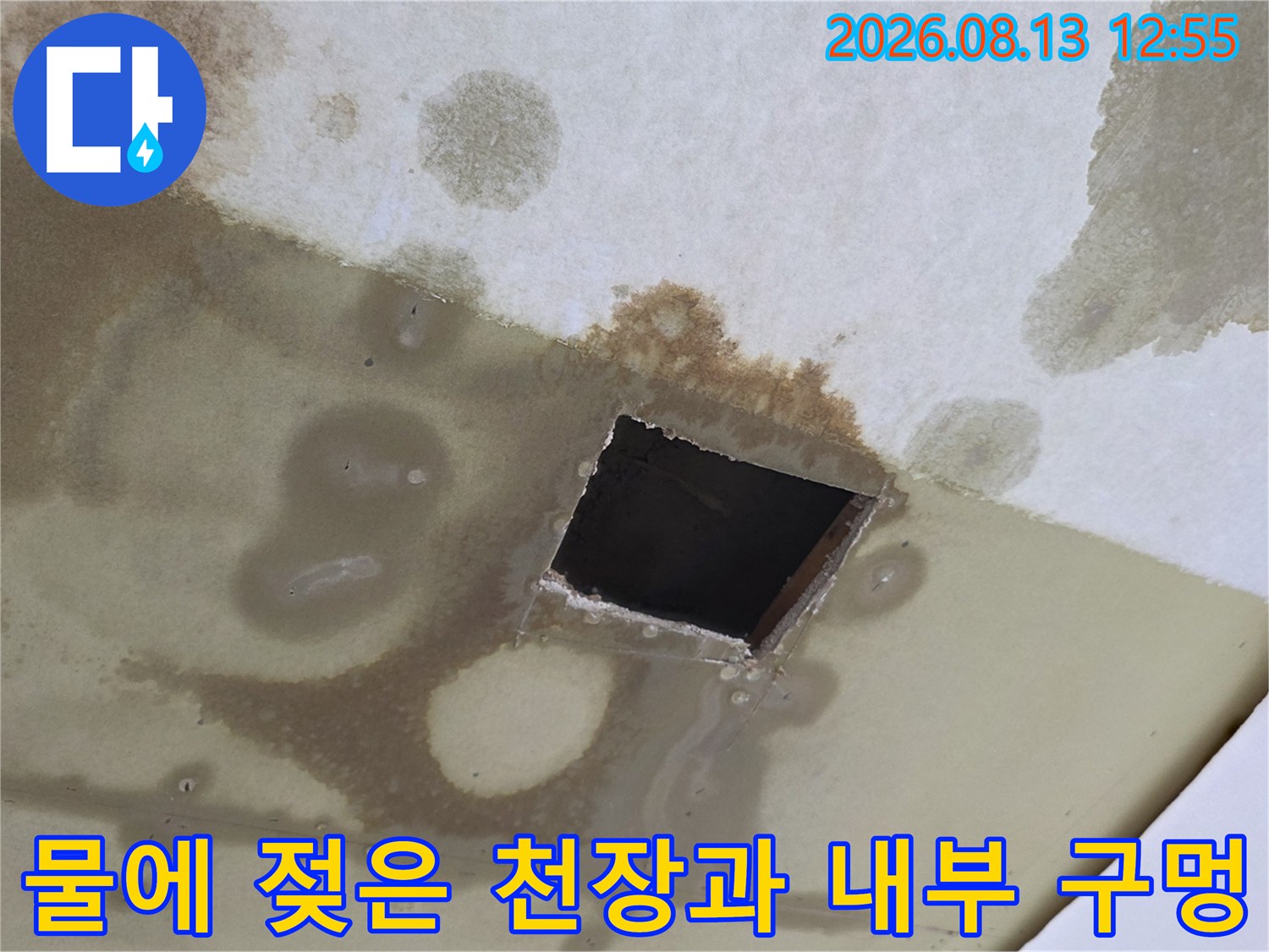 갈색의 누수 얼룩이 퍼져 있는 하얀색 천장지와 정사각형으로 뚫린 공간