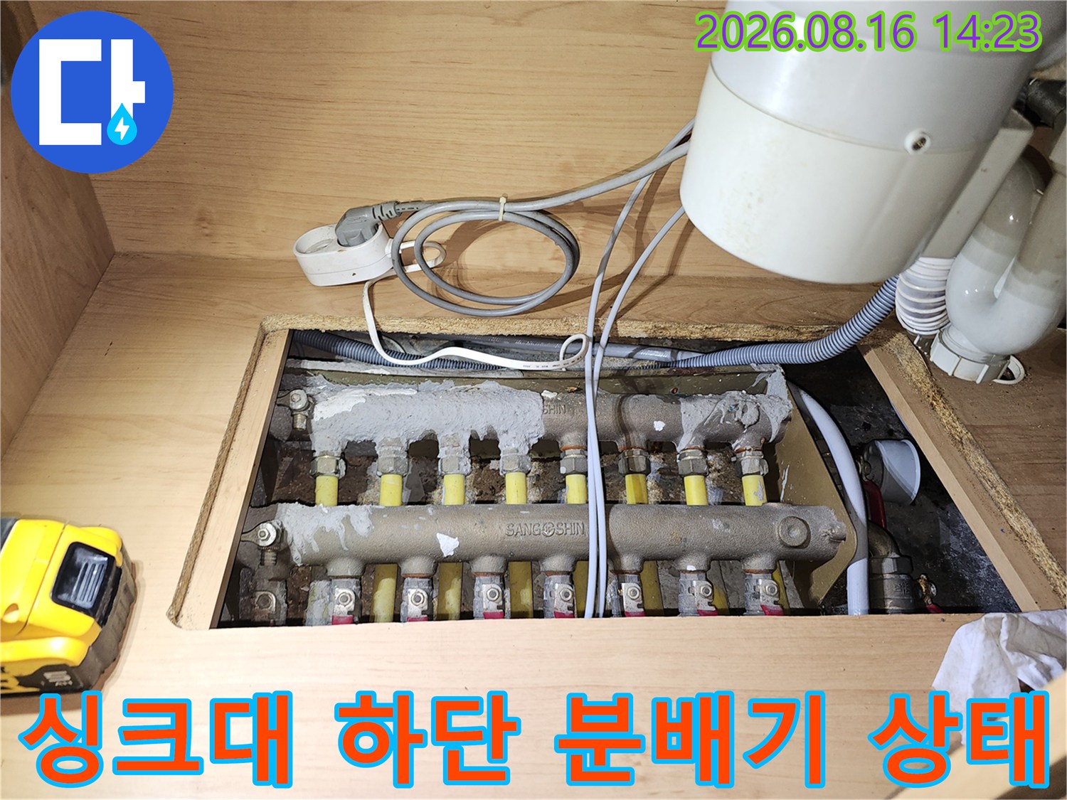 싱크대 밑 공간에 노출된 보일러 분배기와 다수의 배관 연결 부위를 촬영한 사진입니다.