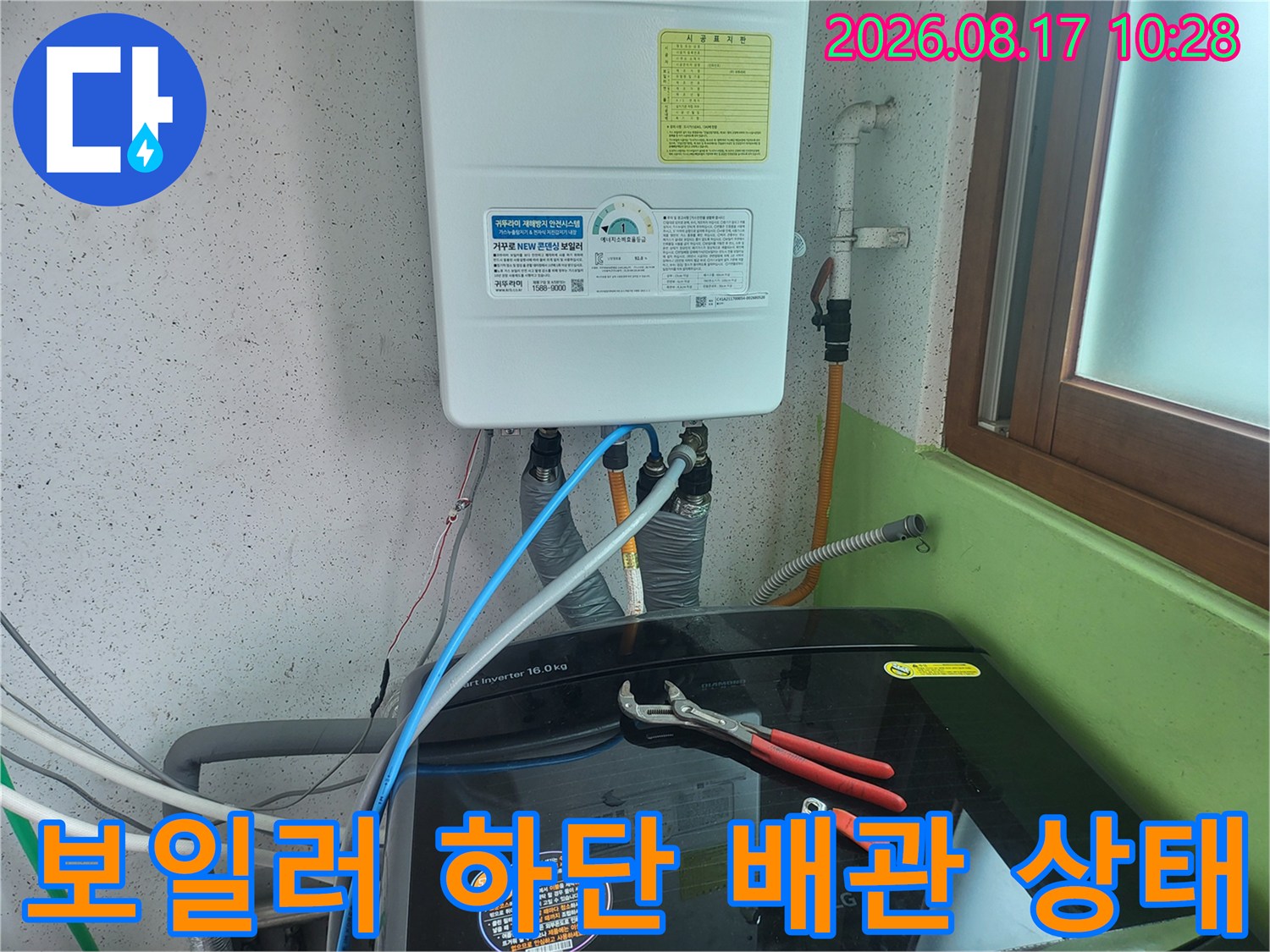 보일러 아래쪽의 밸브와 연결된 호스들을 점검하는 현장 사진입니다.