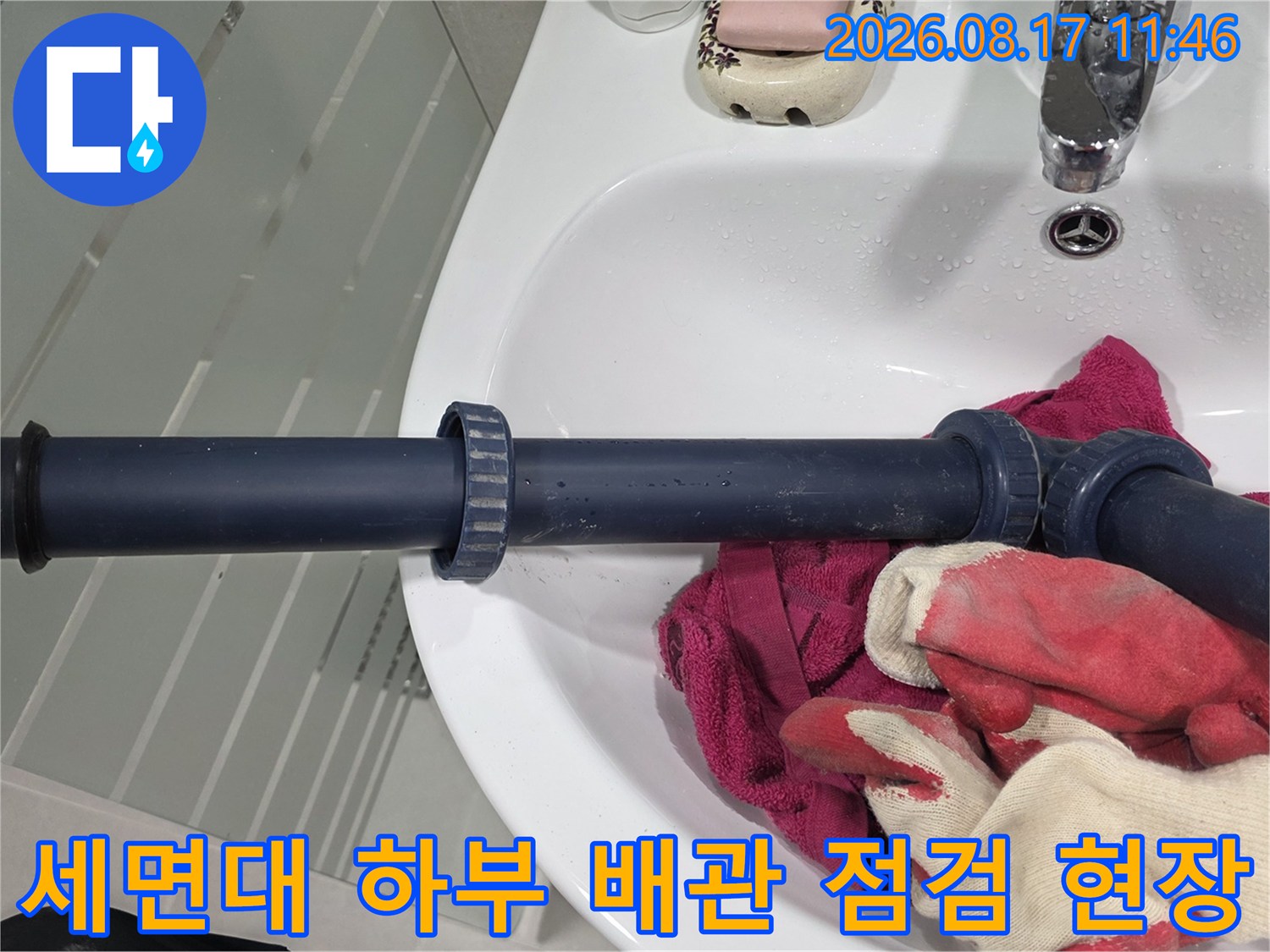 세면대 밑으로 이어지는 검은색 배수 배관과 작업 도구들입니다