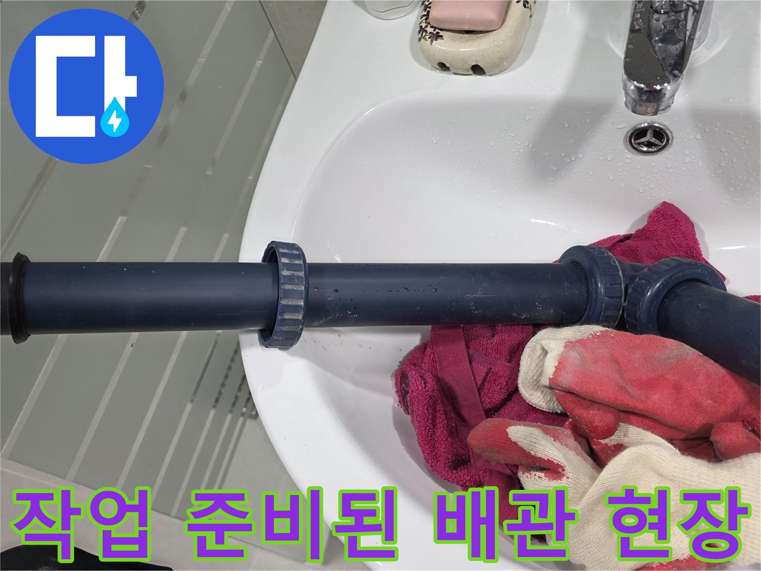 세면대 아래 파란색 배관과 빨간 작업 장갑 사진입니다.