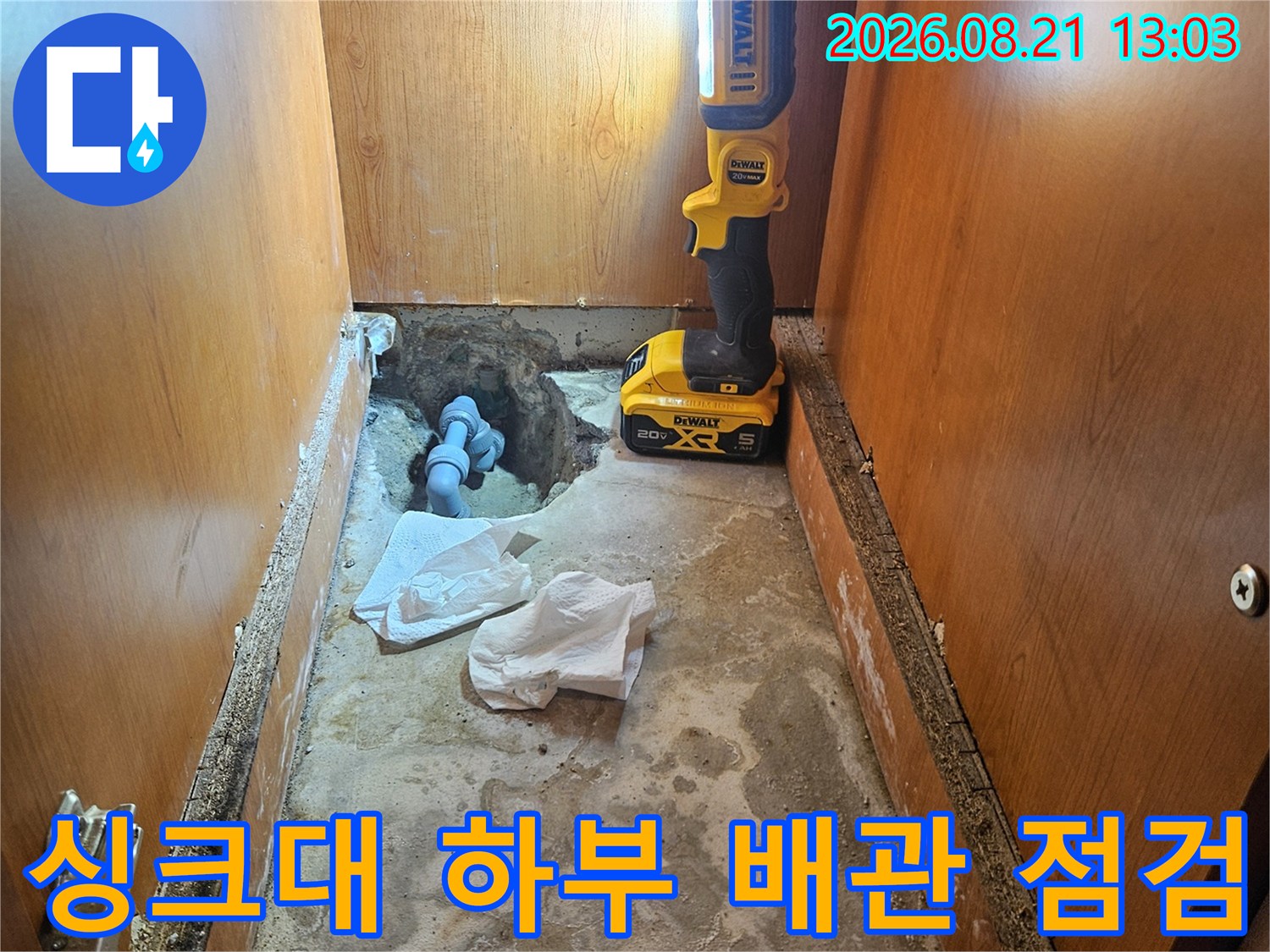손전등으로 비춘 싱크대 하부 벽면의 젖은 배관 상태