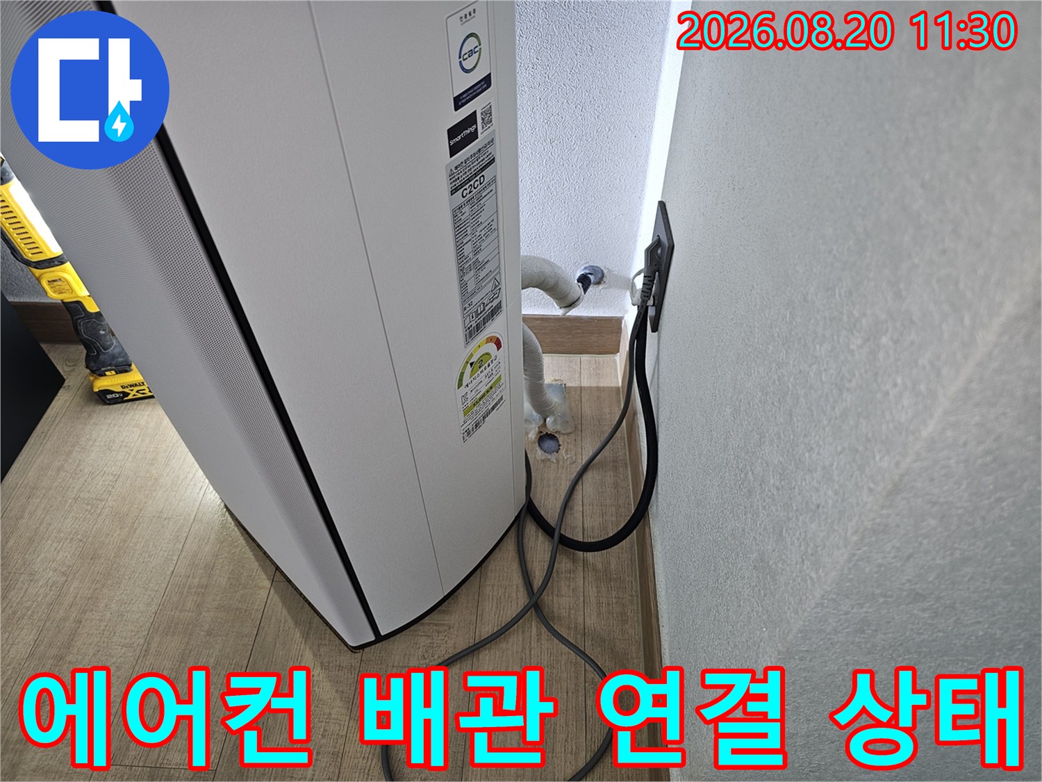 에어컨 실내기 뒤편의 배수 배관과 전원선이 벽면 콘센트에 연결된 모습