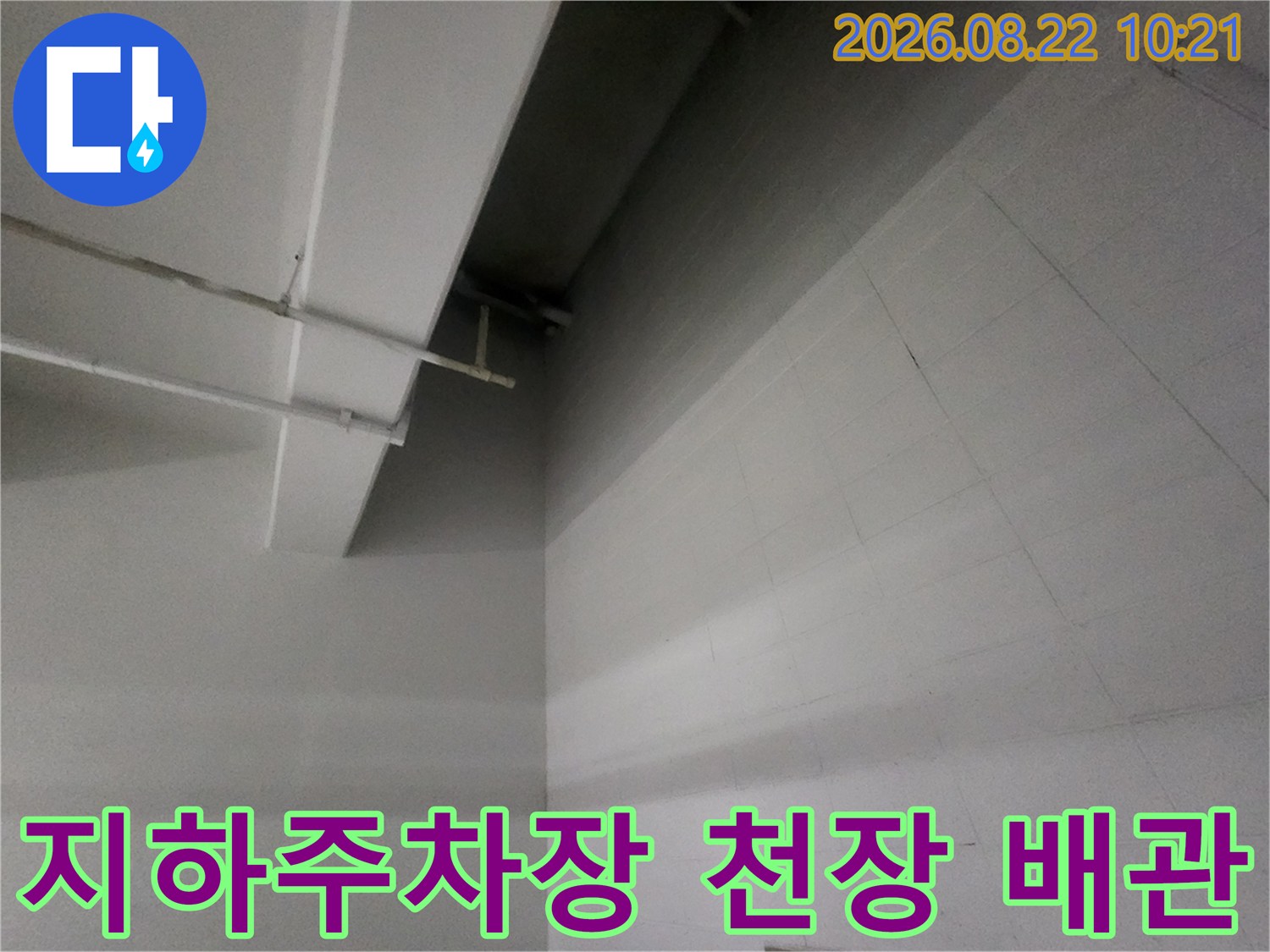 지하주차장-천장에 설치된 하얀색 배관과 타일 벽면 모습입니다.