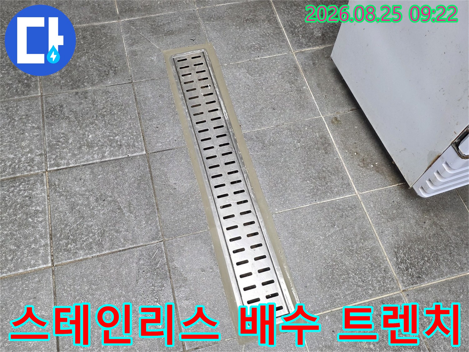 타일 바닥에 설치된 스테인리스 재질의 긴 배수구 트렌치 사진입니다.