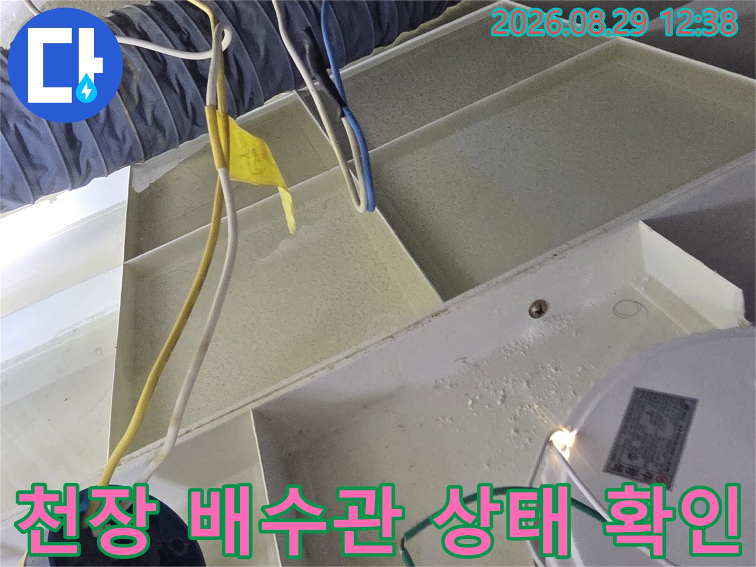 하얀색 천장 구조물 내부의 배관과 전기선들이 얽혀 있는 현장입니다.