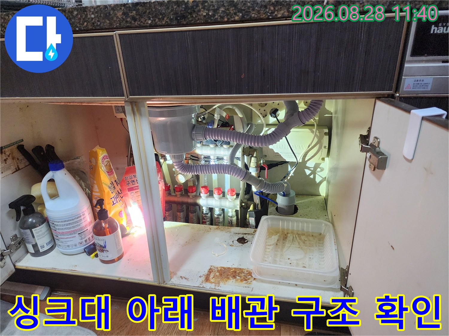 싱크대 하부장 내부의 에어컨 드레인 호스와 주방 배수관 모습