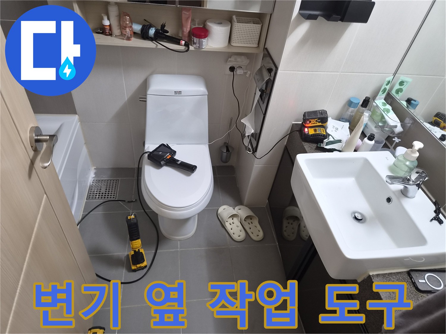 변기 근처 바닥에 놓인 전동 드릴과 점검 장비의 모습입니다.