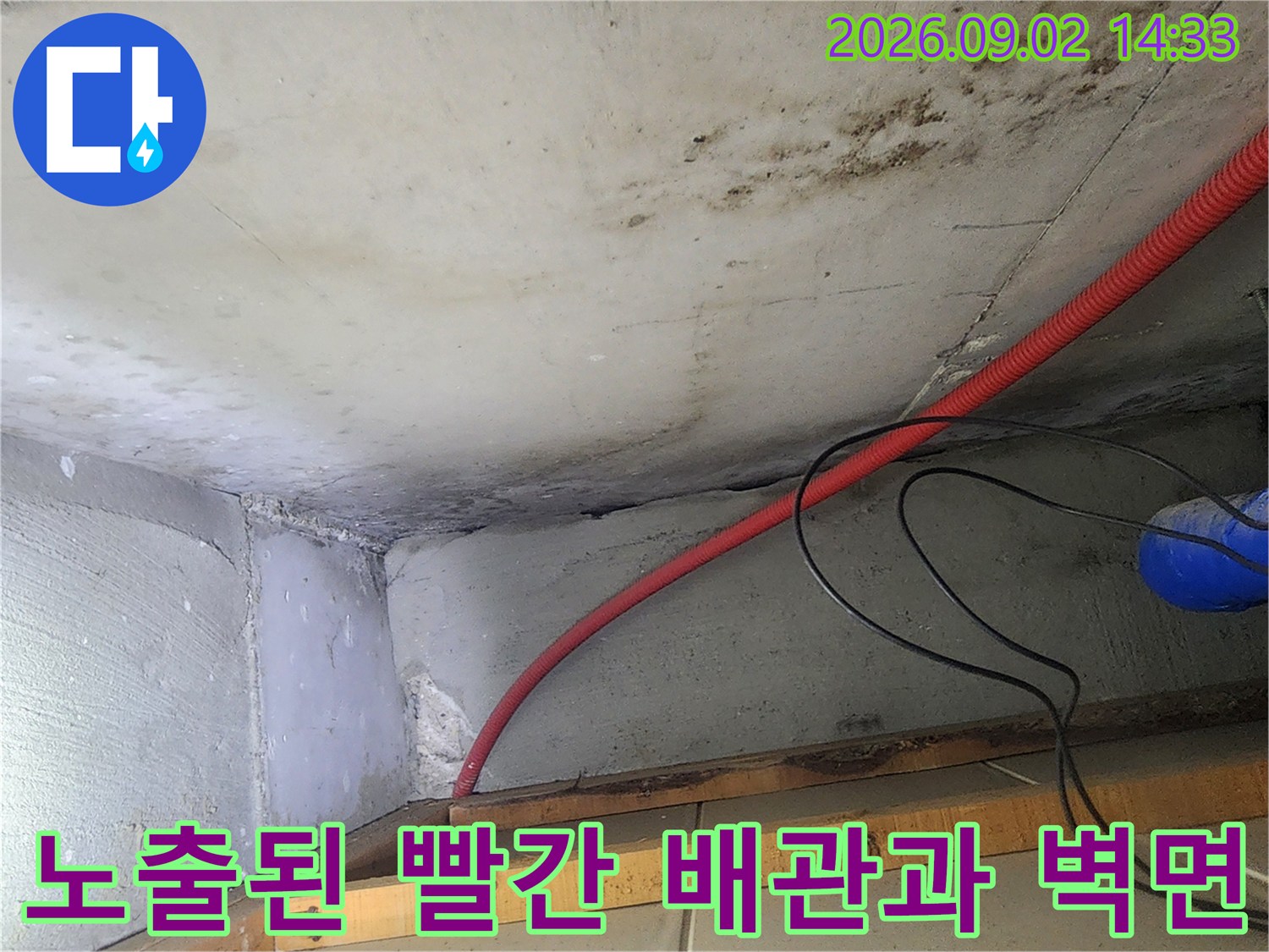 천장 아래로 지나가는 빨간색 주름관 배관과 오염된 콘크리트 벽면