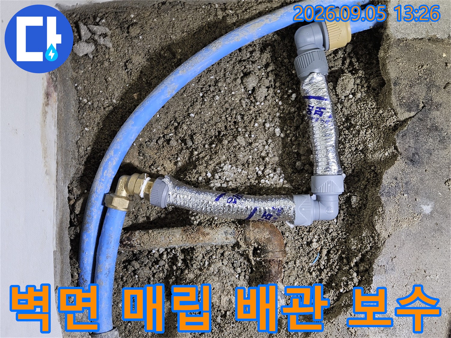 벽체 굴착 부위에 노출된 파란색 수도 배관과 교체용 엘보 부속