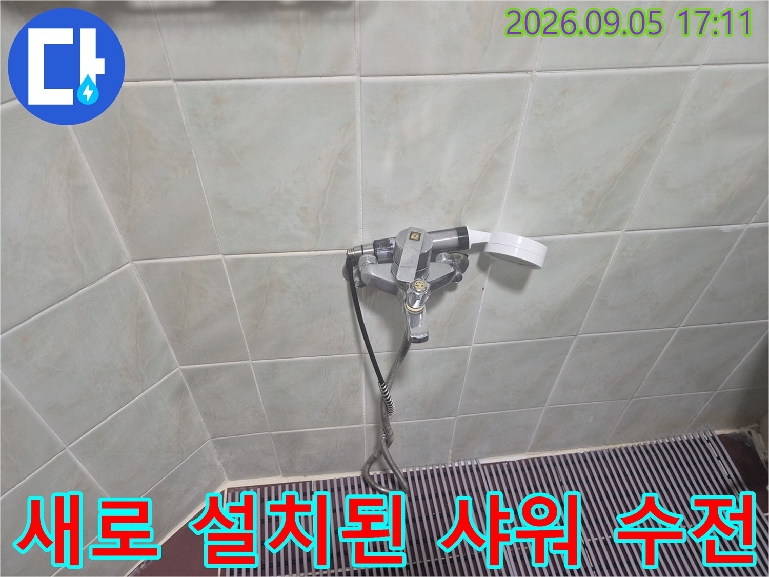 깨끗한 타일 벽면에 설치된 은색 샤워 수전과 호스 연결 부위입니다.