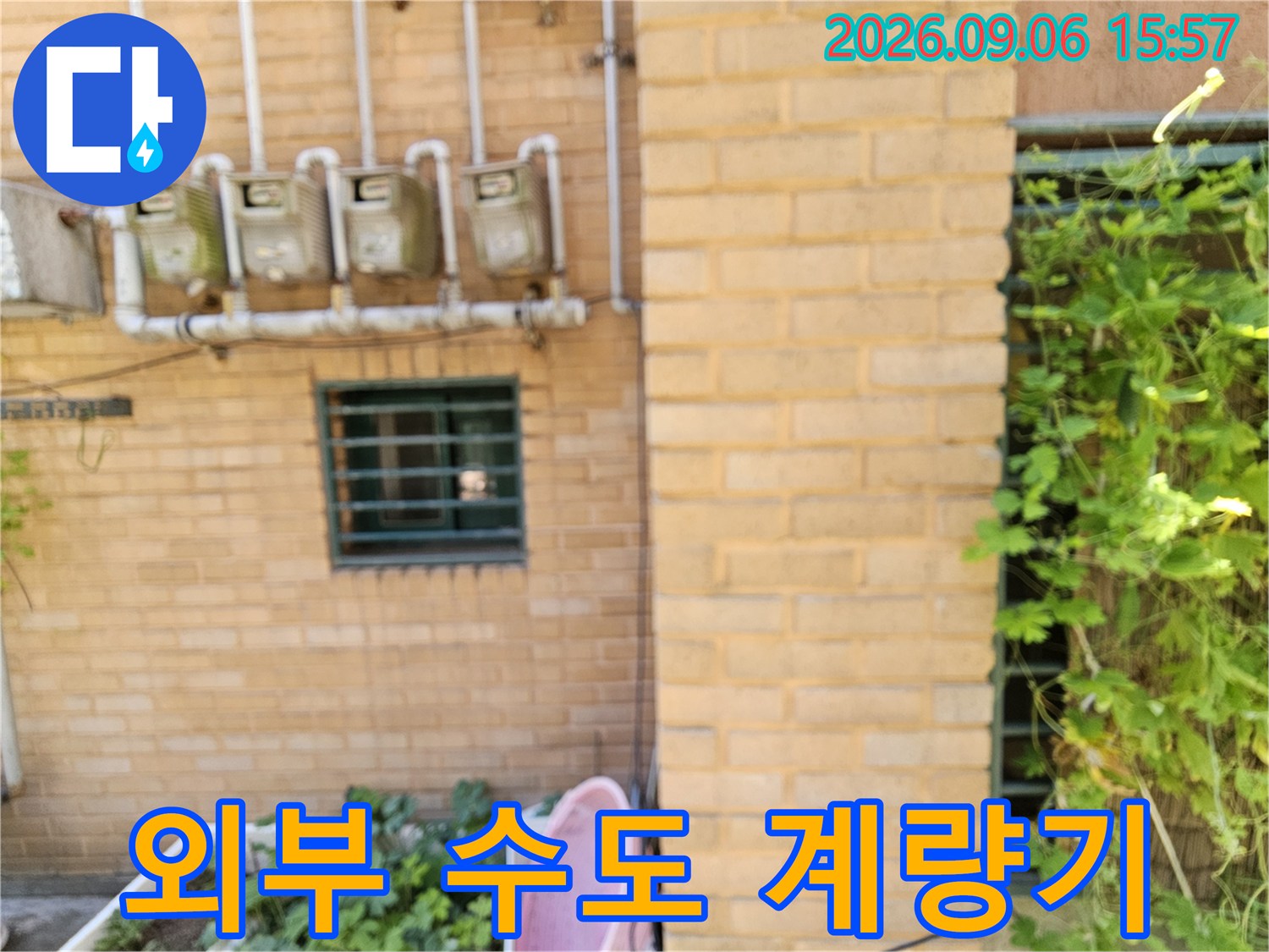 벽돌로 된 외벽에 설치된 수도 계량기와 연결된 관들의 모습입니다.