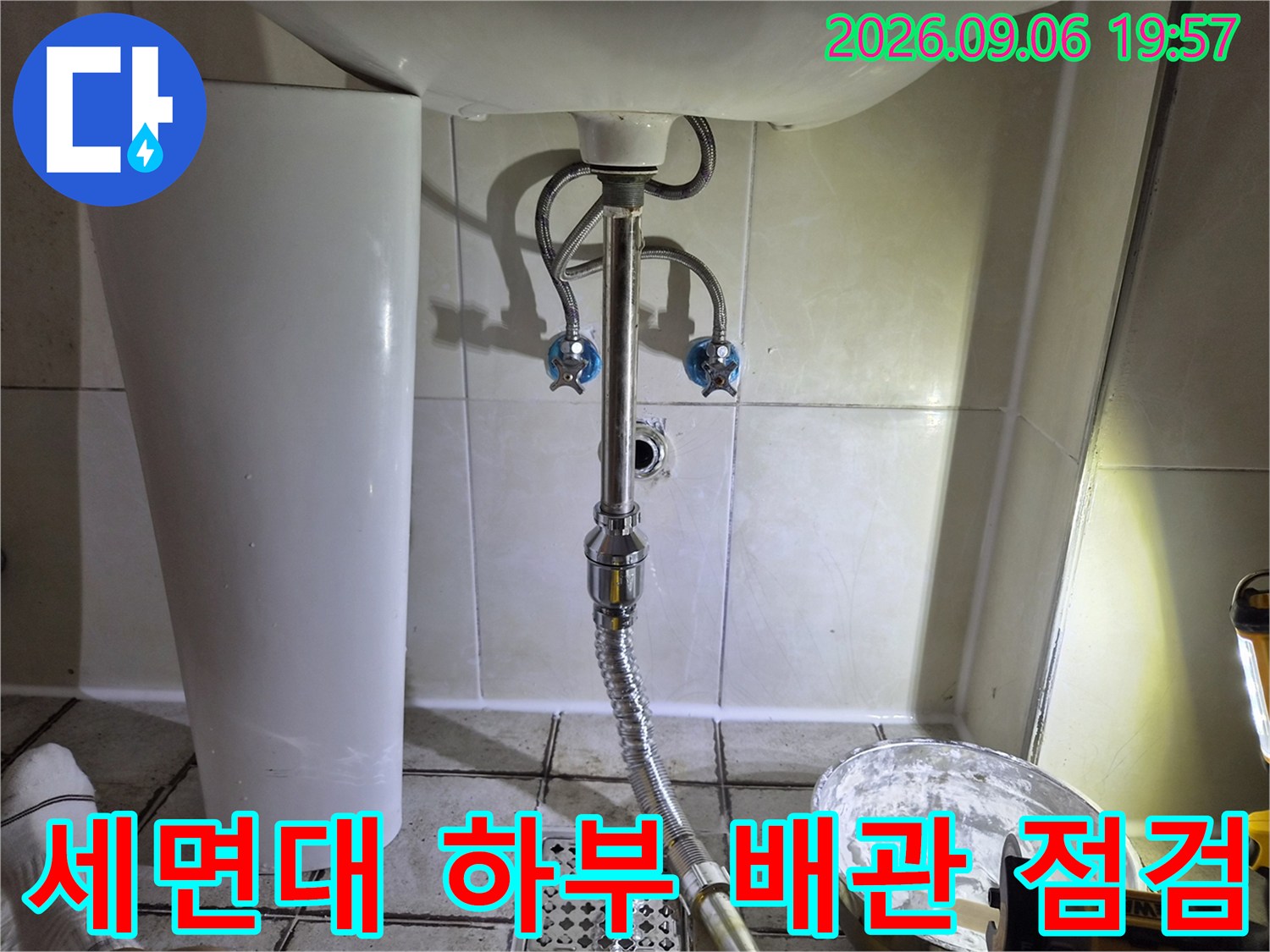 세면대 아래 은색 트랩과 벽면 밸브를 클로즈업한 사진입니다.