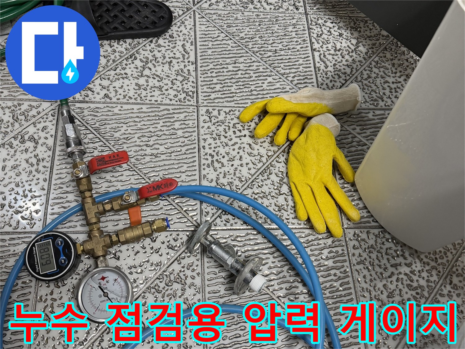 바닥에 놓여 있는 누수 탐지용 압력계와 파청색 호스 및 도구들