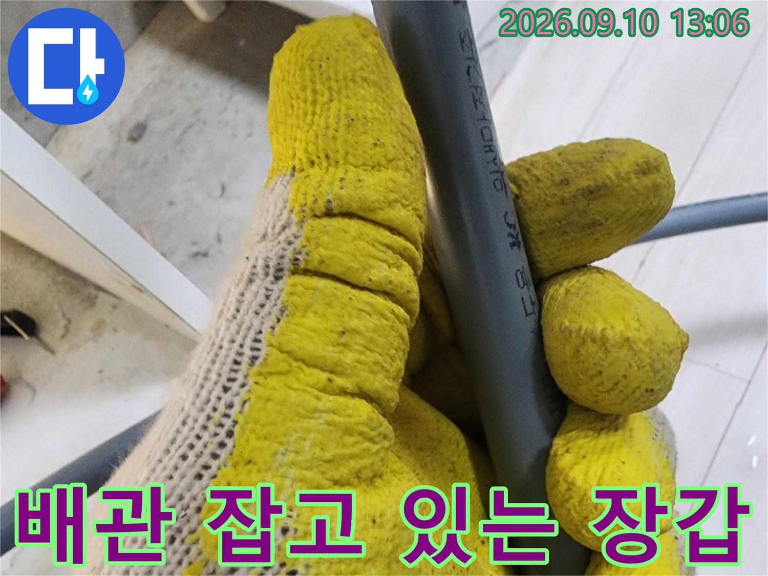 노란색 작업 장갑이 회색 배관을 쥐고 있는 모습