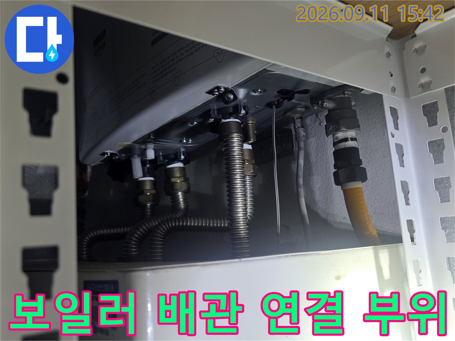 보일러 하부의 금속 호스와 급수 밸브가 있는 배관 구조입니다.