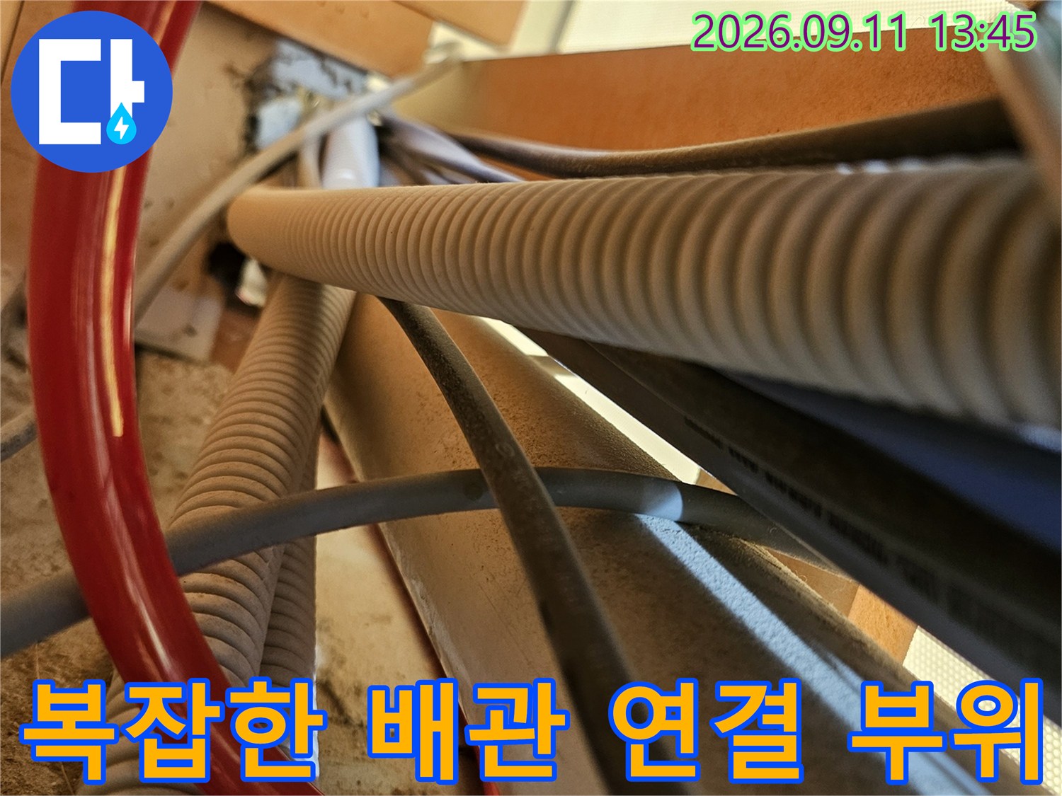 주름진 흰색 배관과 붉은색 호스가 교차하는 현장 사진입니다.