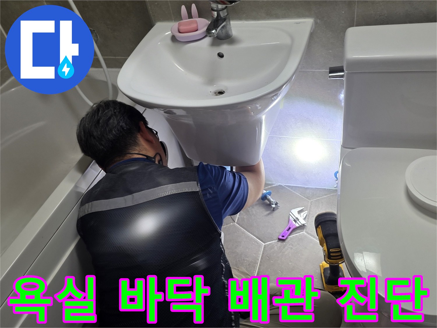 몽키스패너와 장비를 이용해 세면대 하단 배관을 점검하는 장면입니다.