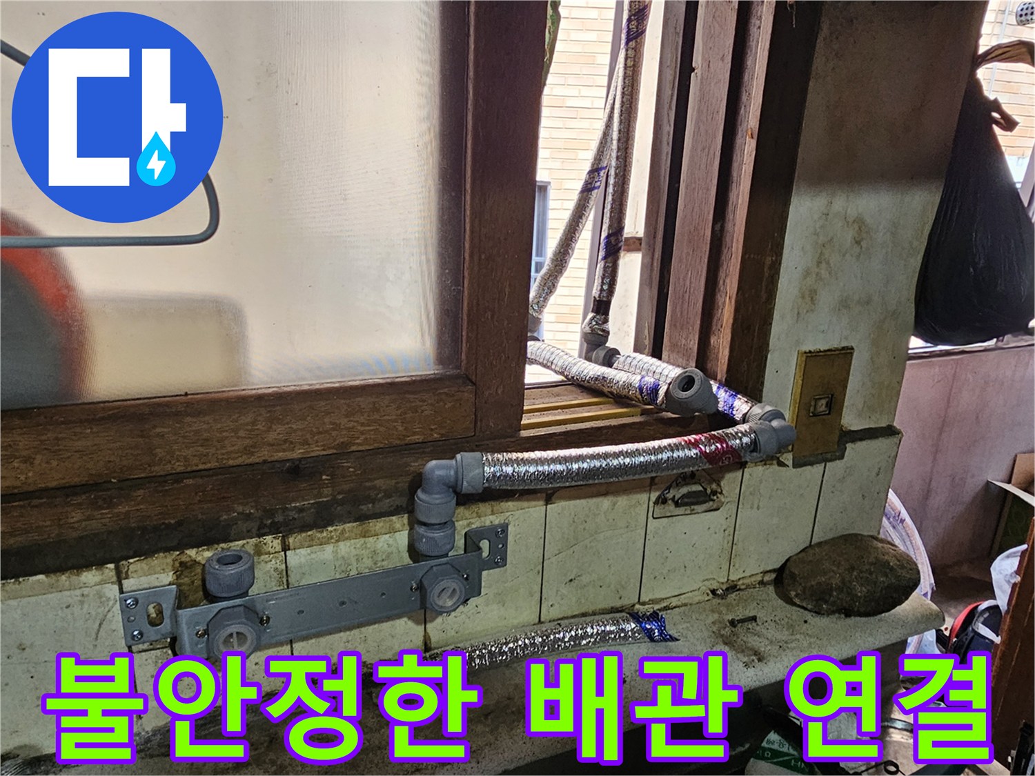 창문 하단 벽면에 설치된 노후된 배관과 연결 부품들의 모습입니다.